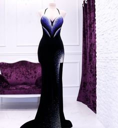 a black and blue dress on display in front of a purple couch with curtains behind it