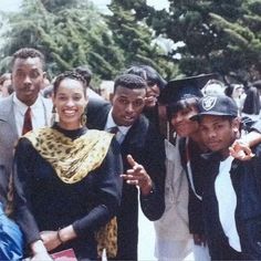 a group of people standing next to each other in front of trees and buildings with one person wearing a graduation cap