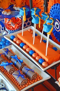 a table topped with cakes and desserts covered in orange frosting, blue decorations