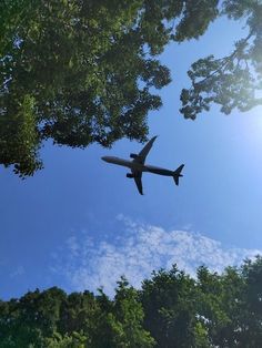 an airplane is flying through the blue sky above some trees and clouds in the background