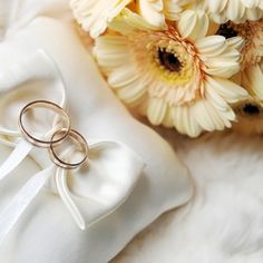 two gold wedding rings sitting on top of a white pillow next to some daisies