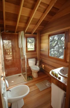 a bathroom with wooden walls and flooring has a toilet, sink, and shower