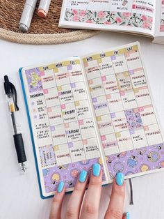 a woman's hand holding a pen and looking at a planner