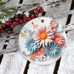 a white ornament with flowers on it sitting in the snow next to berries