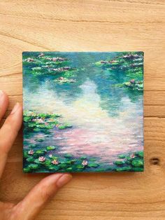 a painting of water lilies on a wooden surface with a hand holding it up