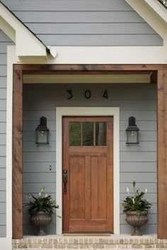 the front door of a house with two planters on the steps and a wooden door