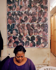 a woman sitting in front of a wall with pictures on it and her hair pulled back