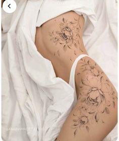 a woman laying on top of a bed covered in white sheets with flowers tattooed on her stomach