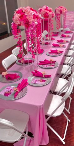 the table is set with pink flowers and silver plates on it, along with white chairs