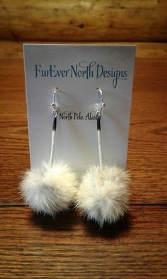 a pair of earrings with white fur on top of a wooden table next to a card