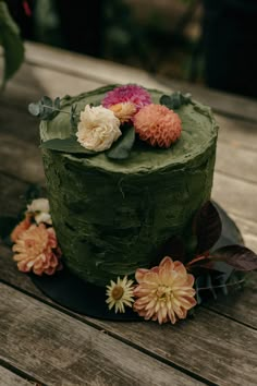 there is a green cake with flowers on the top and bottom layer, sitting on a wooden table