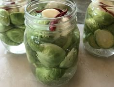 three jars filled with pickles and other vegetables on a table top next to an apple