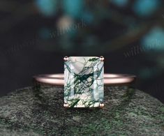 a green and white marble ring sitting on top of a mossy rock with copper accents