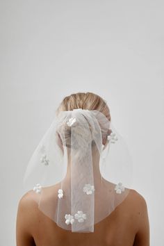 the back of a woman wearing a veil with white flowers on it's head