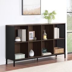 a shelf with books and pictures on it in front of a wall mounted art piece