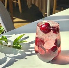 a glass filled with ice and cherries sitting on top of a table next to a plant