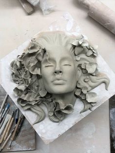 a clay sculpture of a woman's face with flowers in her hair