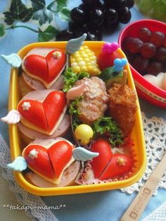 a yellow tray filled with food next to a bowl of grapes and other fruit on top of a blue table cloth