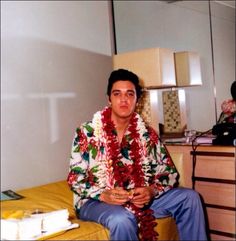 a man sitting on top of a bed next to a wooden dresser in a room