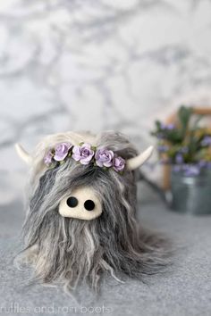 a stuffed animal with long hair and flowers in it's head sitting on the ground