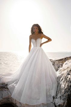 a woman in a wedding dress standing on rocks near the ocean with her hand on her hip