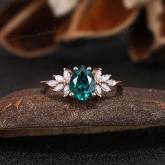 an emerald and diamond ring sitting on top of a piece of wood next to flowers