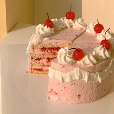 a piece of cake with white frosting and cherries on top is sitting next to the rest of the cake