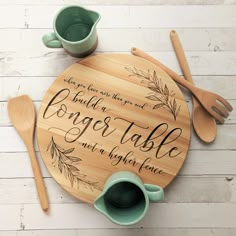 a round wooden table with two mugs and spoons on it that says, build a longer table not a higher place