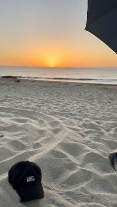 the sun is setting at the beach with an umbrella and hat in the foreground