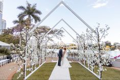 a bride and groom standing in front of an arch with white flowers on the grass