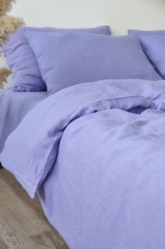 an unmade bed with purple sheets and pillows