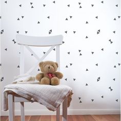 a teddy bear sitting on top of a chair in front of a wall with black arrows