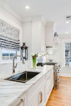 a kitchen with white cabinets and marble counter tops, along with a stainless steel sink