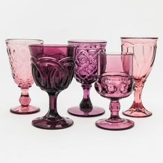 five different colored glass goblets sitting next to each other on a white surface