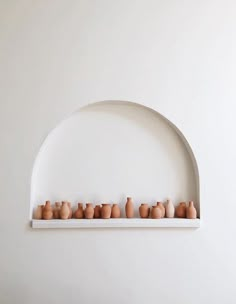 there are many vases lined up on the shelf in front of the white wall