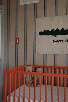 a teddy bear sitting on top of a crib in a room with striped walls