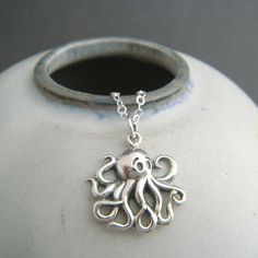 small silver octopus necklace. tiny sterling sea creature pendant. ocean aquatic marine animal cartoon beach jewelry nature charm. 5/8" - A small solid sterling silver octopus, measuring 5/8" (16 mm) across and down. - Necklace is 1.5 mm sterling silver cable chain, with high quality lobster clasp and locking jump rings, all solid sterling silver. Length customizable at drop down menu. - Shiny smooth front, oxidized (blackened) to bring out details. Back is hollowed out, small 925 mark.   - With sustainability in mind, charm is made from 100% post-consumer recycled sterling silver. - Packaged in a modern circular tin, ready for gift giving, and comes with a silver polish pad and care instructions. Customize chain length or "charm only" option: - Charm only option, no chain. Charm does incl Ocean-inspired Sterling Silver Charm Necklaces, Ocean-inspired Silver Sterling Charm Necklaces, Octopus Jewelry, Octopus Necklace, Jewelry Nature, Top Rings, Animal Cartoon, Sea Creature, Marine Animals