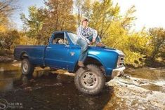 a man sitting on the back of a blue pickup truck in a river with trees around