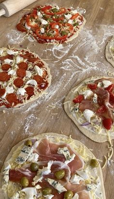 four pizzas with different toppings sitting on top of a wooden table covered in plastic wrap