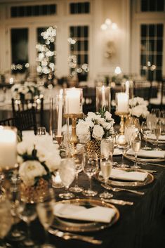 the table is set with white flowers, candles and wine glasses for an elegant dinner