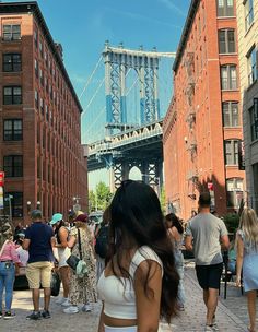 people are walking on the sidewalk in front of tall buildings and a bridge over water