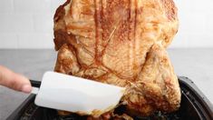 a person cutting up a large piece of meat on top of a black tray with white spatula