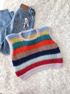 a rainbow sweater and jean shorts are laying on a fluffy white blanket next to a pair of jeans