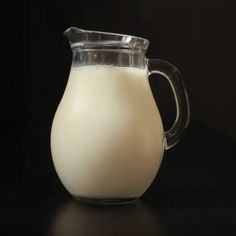 a glass pitcher filled with milk on top of a table