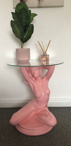 a glass table topped with a pink statue next to a potted plant