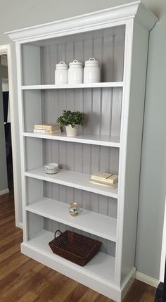 a white bookcase with three shelves and two baskets on the bottom shelf, in a living room