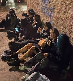 group of people sitting on the side of a building with cell phones in their hands