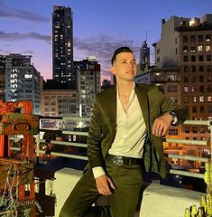 a man sitting on top of a roof next to tall buildings at night with city lights in the background