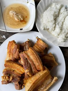 two plates with food on them next to some rice and sauces in bowls behind them