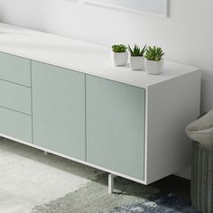 two plants are sitting on top of a white cabinet next to a chair and rug